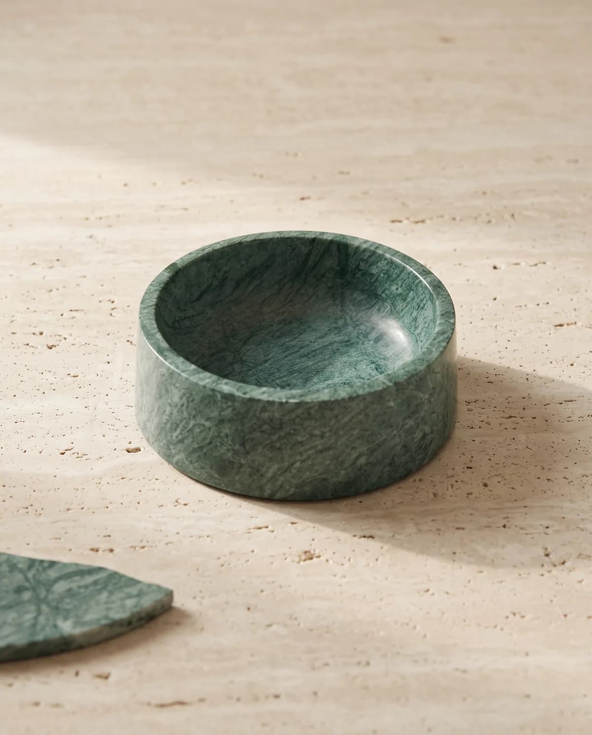 Verde Guatemala marble dog bowl on a travertine slab in soft window light