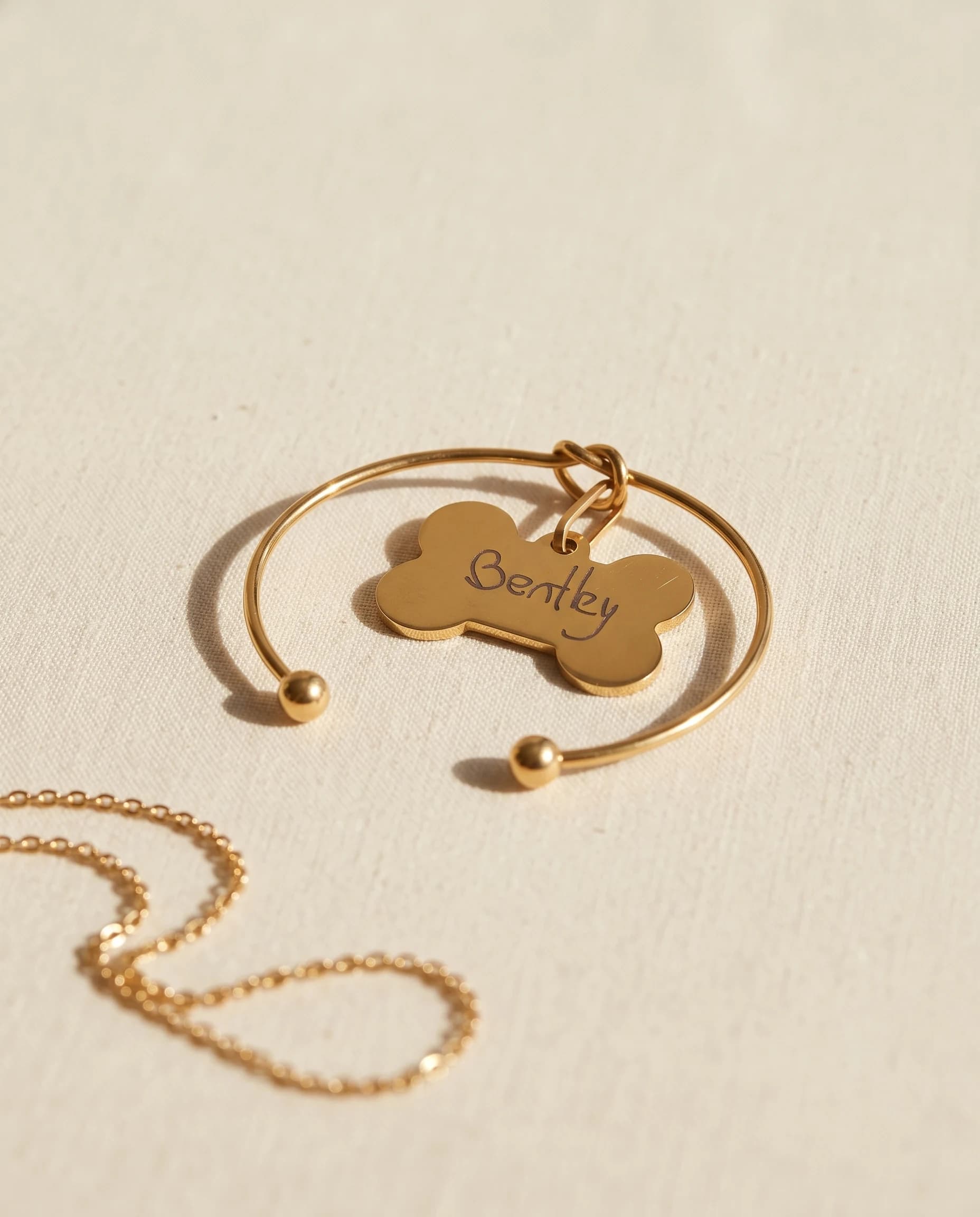 Open gold-plated bangle with ball ends and a miniature bone tag engraved Bentley