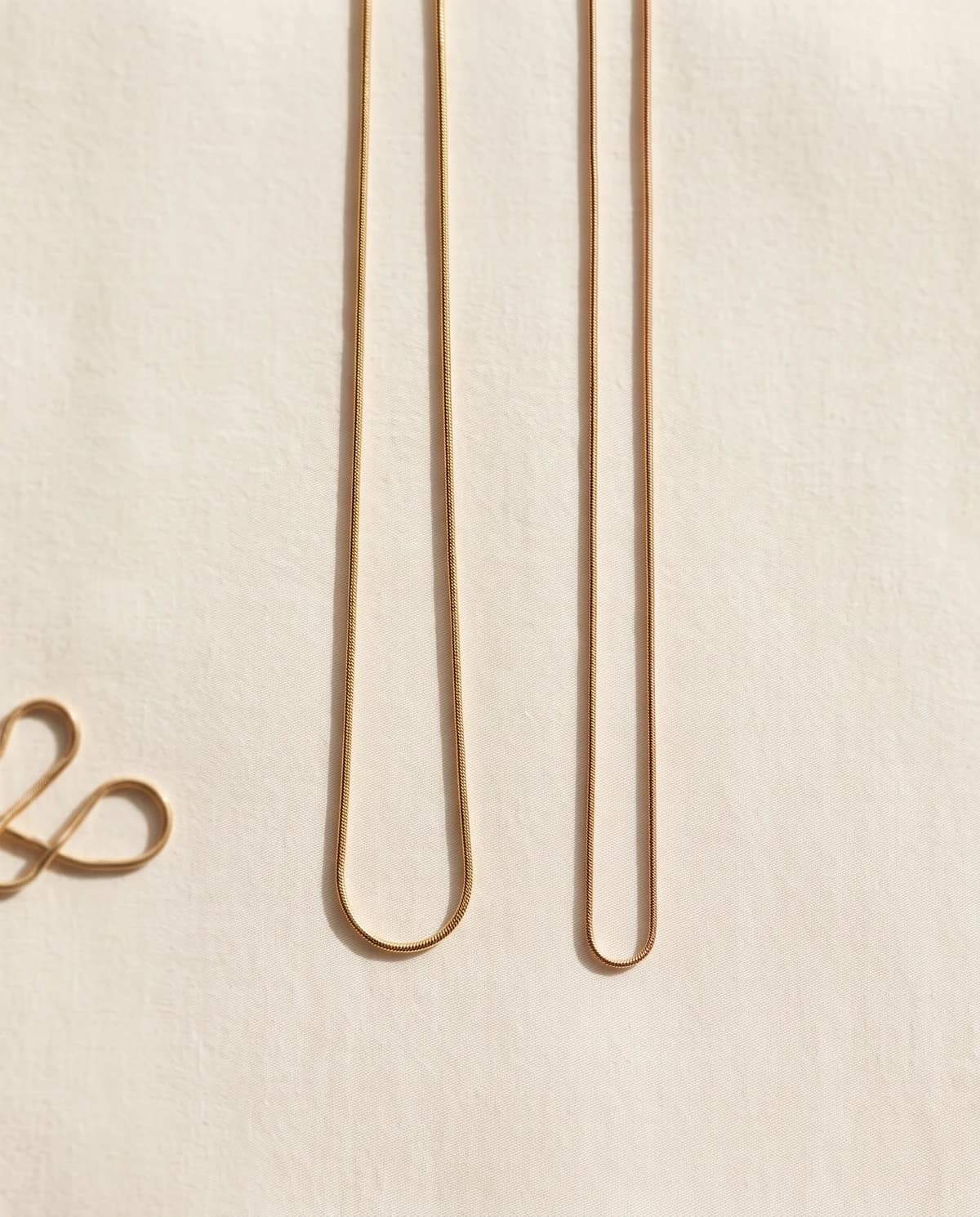 Two gold-plated snake chains for the matching owner necklace, laid on bone linen