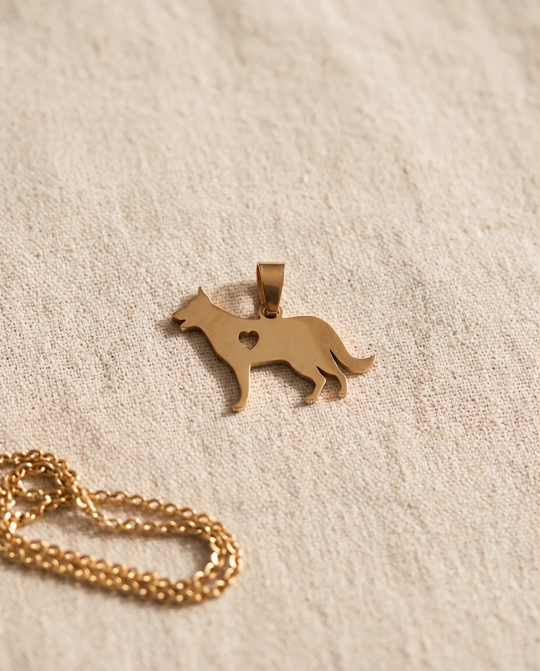 Gold-plated dog silhouette pendant with a heart cut-out, on bone linen