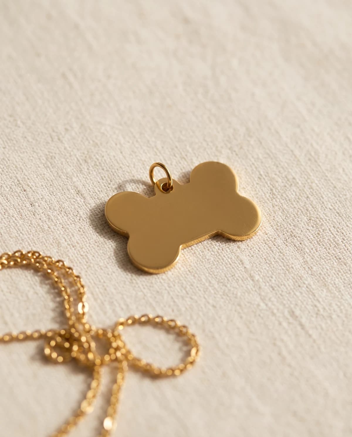 Gold-plated bone-shaped dog tag on bone linen, polished blank face ready for engraving