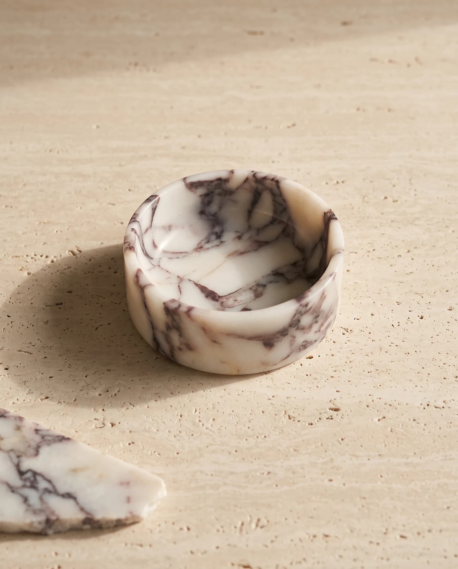 Calacatta Viola marble dog bowl on a travertine slab in soft window light