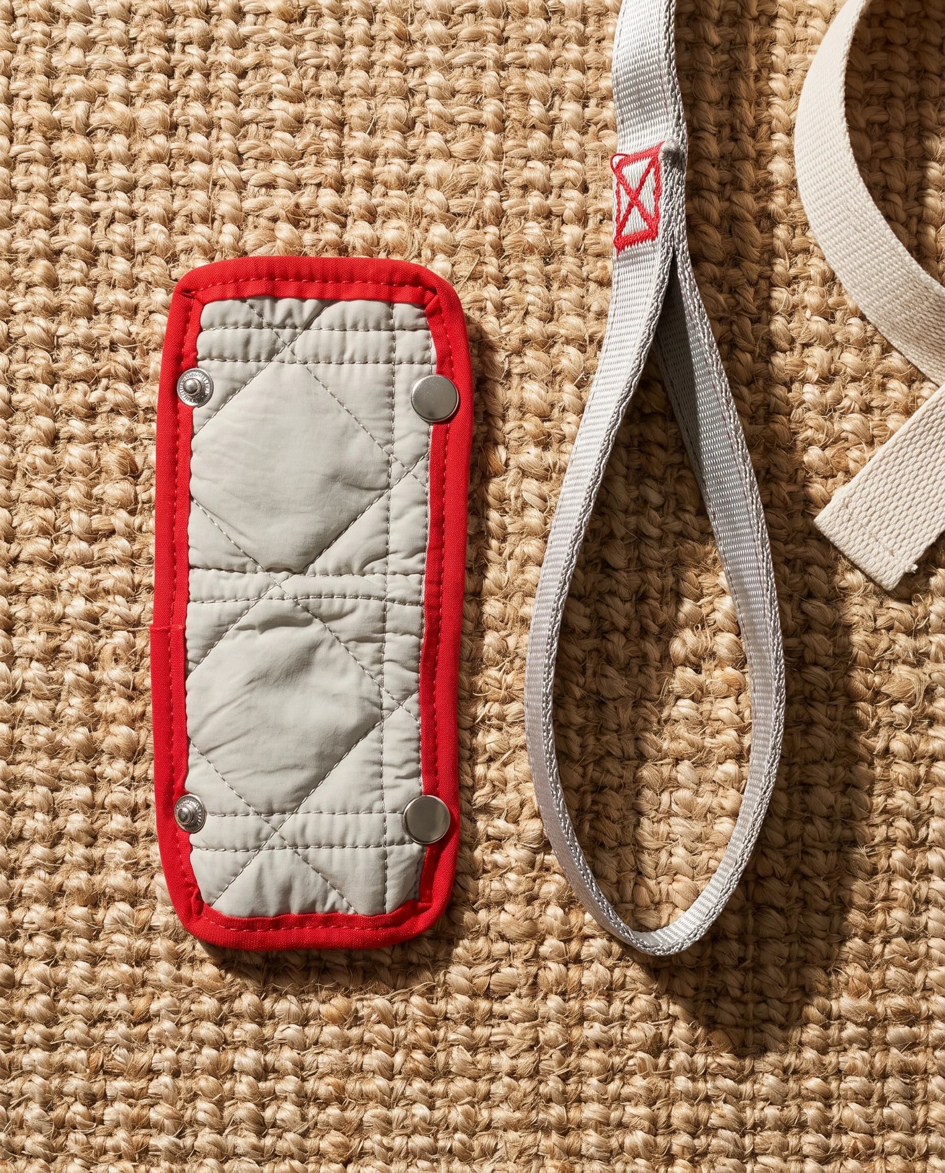 Quilted handle cover with red binding on a jute mat, beside the leash handle loop
